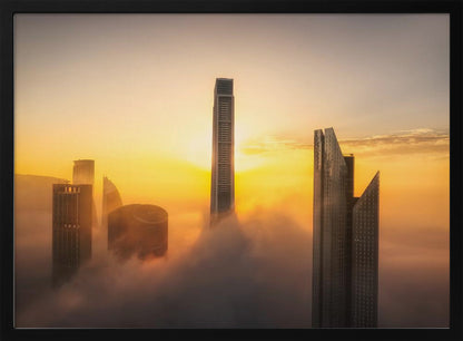 A framed photograph of a modern city skyline with skyscrapers emerging from a thick layer of clouds at sunrise, creating a dramatic and ethereal scene against a golden sky. Wall Art