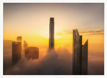 A framed photograph of a modern city skyline with skyscrapers emerging from a thick layer of clouds at sunrise, creating a dramatic and ethereal scene against a golden sky. Wall Art
