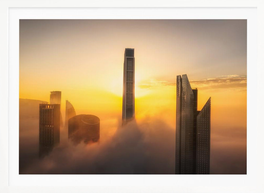 A framed photograph of a modern city skyline with skyscrapers emerging from a thick layer of clouds at sunrise, creating a dramatic and ethereal scene against a golden sky. Wall Art