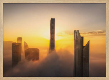 A framed photograph of a modern city skyline with skyscrapers emerging from a thick layer of clouds at sunrise, creating a dramatic and ethereal scene against a golden sky. Wall Art