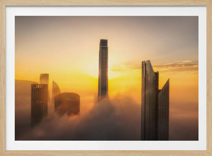 A framed photograph of a modern city skyline with skyscrapers emerging from a thick layer of clouds at sunrise, creating a dramatic and ethereal scene against a golden sky. Wall Art