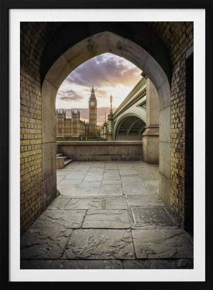 A scenic view of London's Big Ben clock tower and the Houses of Parliament as seen through a weathered stone archway. The foreground features a stone-paved walkway, and the background shows the iconic landmarks against a cloudy sunset sky with hues of purple and orange. Poster