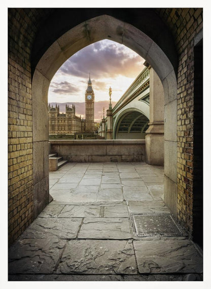 A scenic view of London's Big Ben clock tower and the Houses of Parliament as seen through a weathered stone archway. The foreground features a stone-paved walkway, and the background shows the iconic landmarks against a cloudy sunset sky with hues of purple and orange. Poster