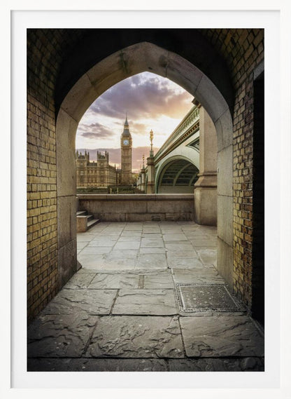 A scenic view of London's Big Ben clock tower and the Houses of Parliament as seen through a weathered stone archway. The foreground features a stone-paved walkway, and the background shows the iconic landmarks against a cloudy sunset sky with hues of purple and orange. Poster
