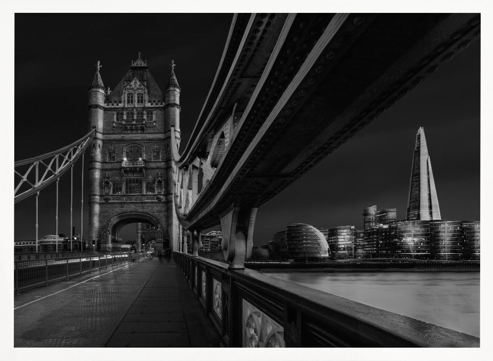 A dramatic, low-angle black and white photograph of London's Tower Bridge at night, taken from the pedestrian walkway. The image showcases the architectural details of the bridge and the illuminated modern city skyline, including The Shard, across the River Thames. Print