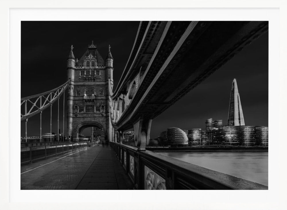 A dramatic, low-angle black and white photograph of London's Tower Bridge at night, taken from the pedestrian walkway. The image showcases the architectural details of the bridge and the illuminated modern city skyline, including The Shard, across the River Thames. Print