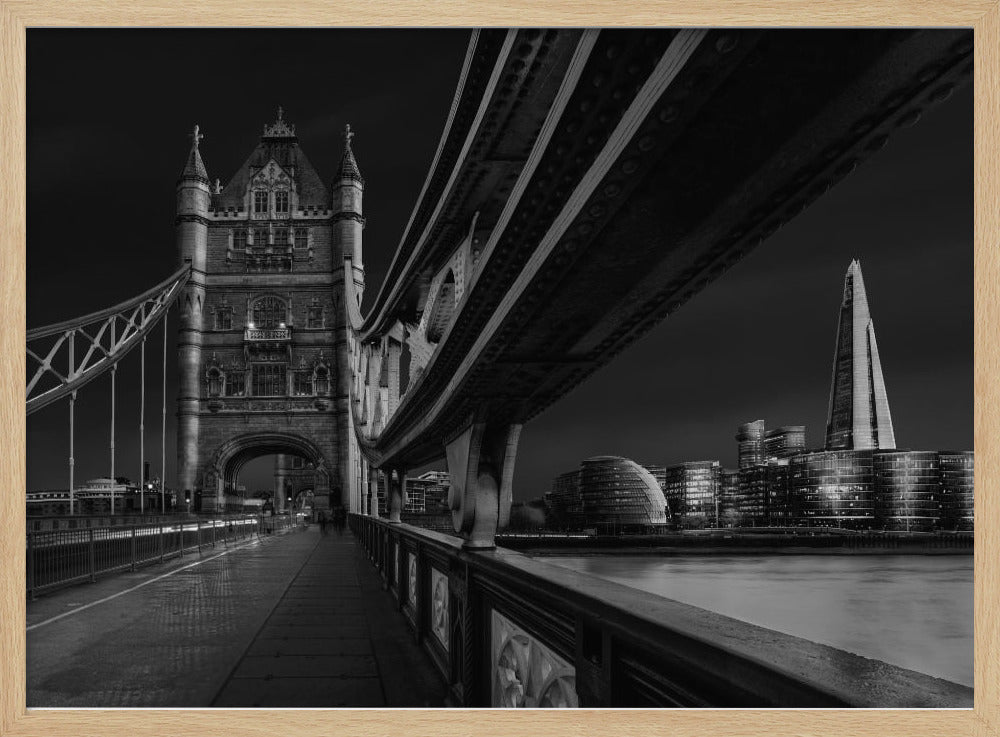 A dramatic, low-angle black and white photograph of London's Tower Bridge at night, taken from the pedestrian walkway. The image showcases the architectural details of the bridge and the illuminated modern city skyline, including The Shard, across the River Thames. Print