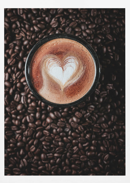 A top-down view of a cappuccino in a black mug with a white heart-shaped foam art design, placed on a bed of dark roasted coffee beans. Artwork