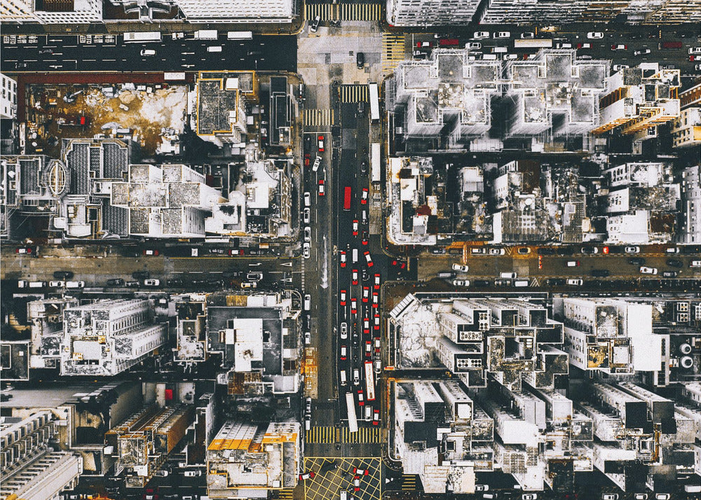 A framed, top-down aerial photo of a dense city grid. The monochromatic scene of white rooftops and dark streets is punctuated by the red and white cars creating lines of traffic below. Decor