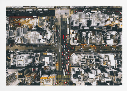 A framed, top-down aerial photo of a dense city grid. The monochromatic scene of white rooftops and dark streets is punctuated by the red and white cars creating lines of traffic below. Decor