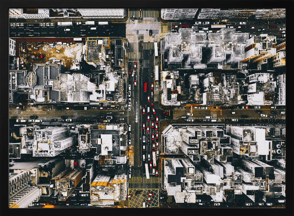 A framed, top-down aerial photo of a dense city grid. The monochromatic scene of white rooftops and dark streets is punctuated by the red and white cars creating lines of traffic below. Decor