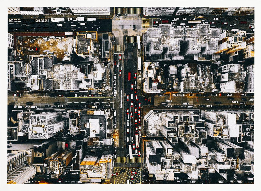 A framed, top-down aerial photo of a dense city grid. The monochromatic scene of white rooftops and dark streets is punctuated by the red and white cars creating lines of traffic below. Decor