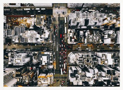 A framed, top-down aerial photo of a dense city grid. The monochromatic scene of white rooftops and dark streets is punctuated by the red and white cars creating lines of traffic below. Decor