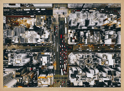 A framed, top-down aerial photo of a dense city grid. The monochromatic scene of white rooftops and dark streets is punctuated by the red and white cars creating lines of traffic below. Decor