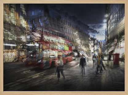A long-exposure, artistic photograph of a busy London street at night. The motion of a red double-decker bus and pedestrians creates a blurred, ghost-like effect, capturing the vibrant energy of the city. The scene is illuminated by streetlights and building windows, all set within a silver frame. Artwork