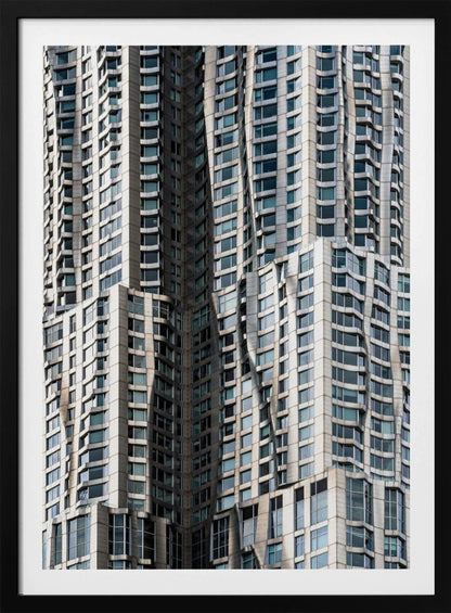 A close-up photograph of the facade of a modern skyscraper with an undulating, wave-like metallic exterior. The building is filled with windows that reflect the light, creating a dynamic pattern of highlights and shadows, all captured within a black frame. Print