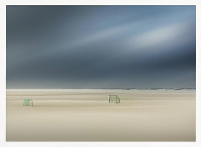A minimalist long-exposure photograph of a vast, empty beach under a dark, moody sky. Two small, solitary soccer goals sit on the pale sand, with the ocean visible as a thin line in the distance. The artwork is presented in a silver frame. Artwork