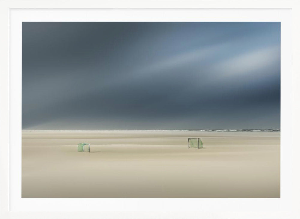 A minimalist long-exposure photograph of a vast, empty beach under a dark, moody sky. Two small, solitary soccer goals sit on the pale sand, with the ocean visible as a thin line in the distance. The artwork is presented in a silver frame. Artwork