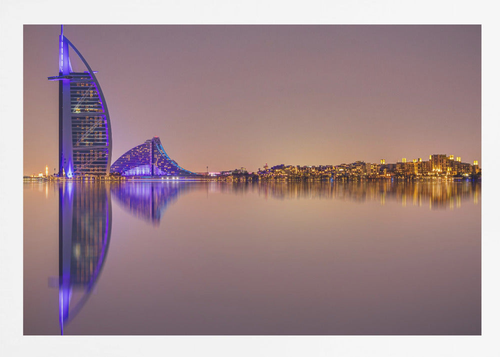 A framed panoramic night photograph of the Dubai skyline featuring the Burj Al Arab hotel lit up in brilliant purple. The city lights and architecture are perfectly reflected in the calm water in the foreground, all under a hazy, dusky sky. Poster