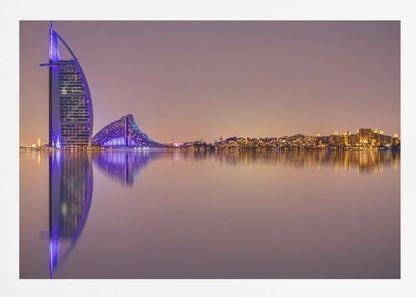 A framed panoramic night photograph of the Dubai skyline featuring the Burj Al Arab hotel lit up in brilliant purple. The city lights and architecture are perfectly reflected in the calm water in the foreground, all under a hazy, dusky sky. Poster
