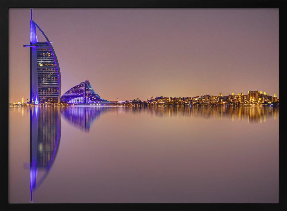 A framed panoramic night photograph of the Dubai skyline featuring the Burj Al Arab hotel lit up in brilliant purple. The city lights and architecture are perfectly reflected in the calm water in the foreground, all under a hazy, dusky sky. Poster