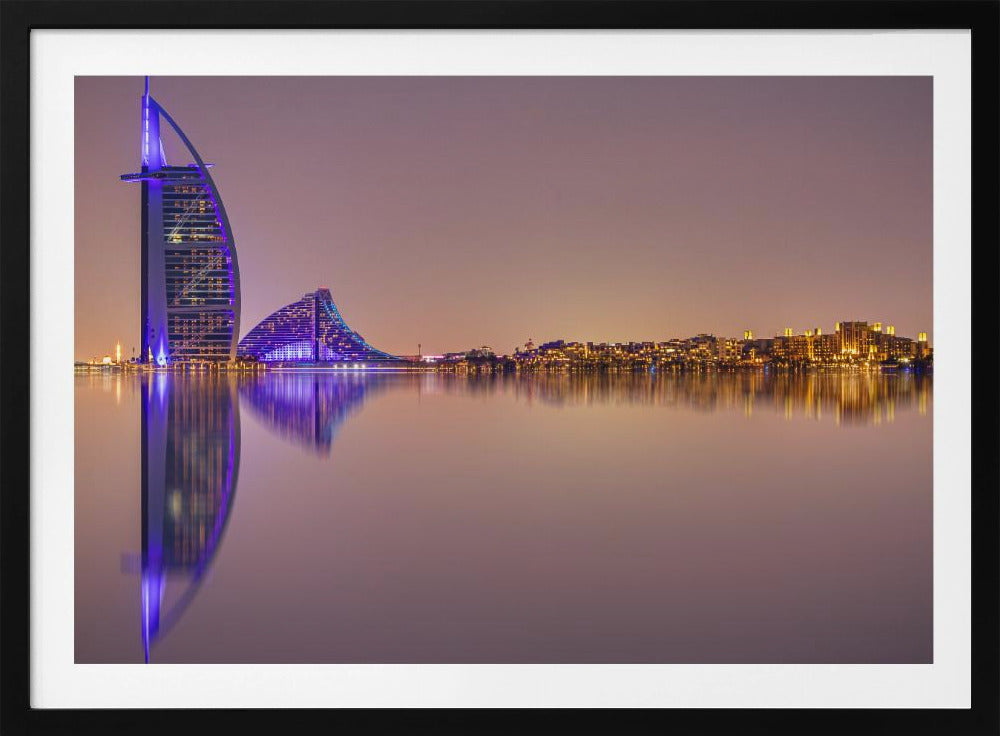 A framed panoramic night photograph of the Dubai skyline featuring the Burj Al Arab hotel lit up in brilliant purple. The city lights and architecture are perfectly reflected in the calm water in the foreground, all under a hazy, dusky sky. Poster