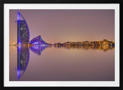 A framed panoramic night photograph of the Dubai skyline featuring the Burj Al Arab hotel lit up in brilliant purple. The city lights and architecture are perfectly reflected in the calm water in the foreground, all under a hazy, dusky sky. Poster
