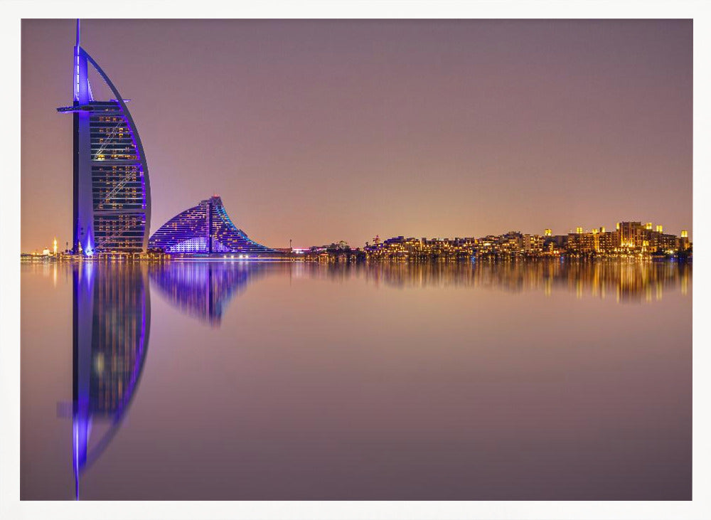 A framed panoramic night photograph of the Dubai skyline featuring the Burj Al Arab hotel lit up in brilliant purple. The city lights and architecture are perfectly reflected in the calm water in the foreground, all under a hazy, dusky sky. Poster
