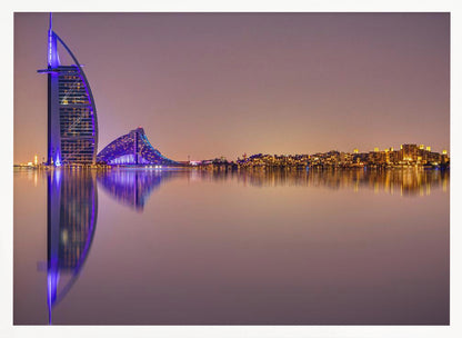 A framed panoramic night photograph of the Dubai skyline featuring the Burj Al Arab hotel lit up in brilliant purple. The city lights and architecture are perfectly reflected in the calm water in the foreground, all under a hazy, dusky sky. Poster
