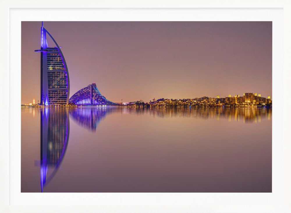 A framed panoramic night photograph of the Dubai skyline featuring the Burj Al Arab hotel lit up in brilliant purple. The city lights and architecture are perfectly reflected in the calm water in the foreground, all under a hazy, dusky sky. Poster