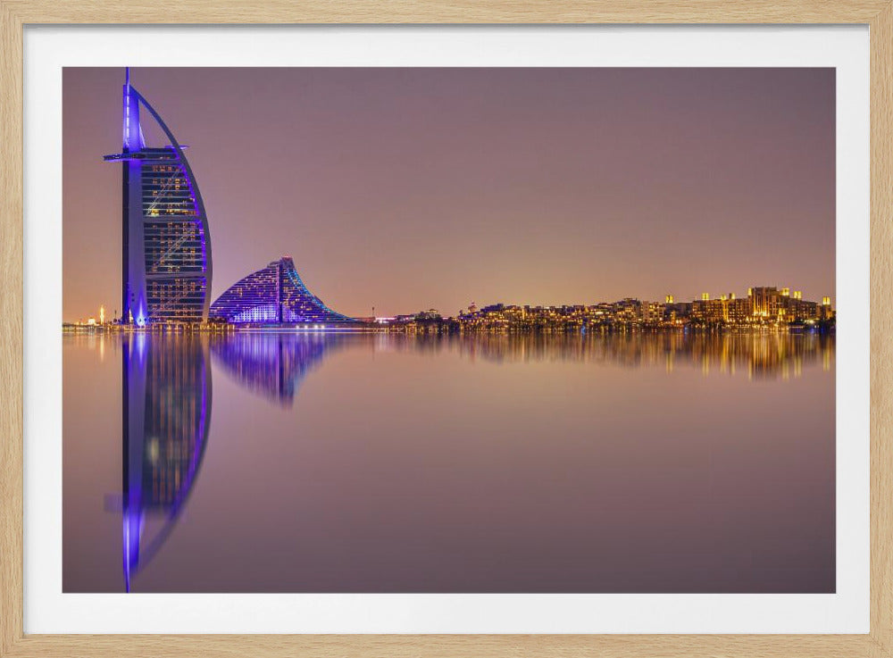 A framed panoramic night photograph of the Dubai skyline featuring the Burj Al Arab hotel lit up in brilliant purple. The city lights and architecture are perfectly reflected in the calm water in the foreground, all under a hazy, dusky sky. Poster