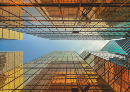 A low-angle, upward view of modern skyscrapers with golden reflective glass windows, creating a geometric pattern against a narrow strip of clear blue sky. Decor