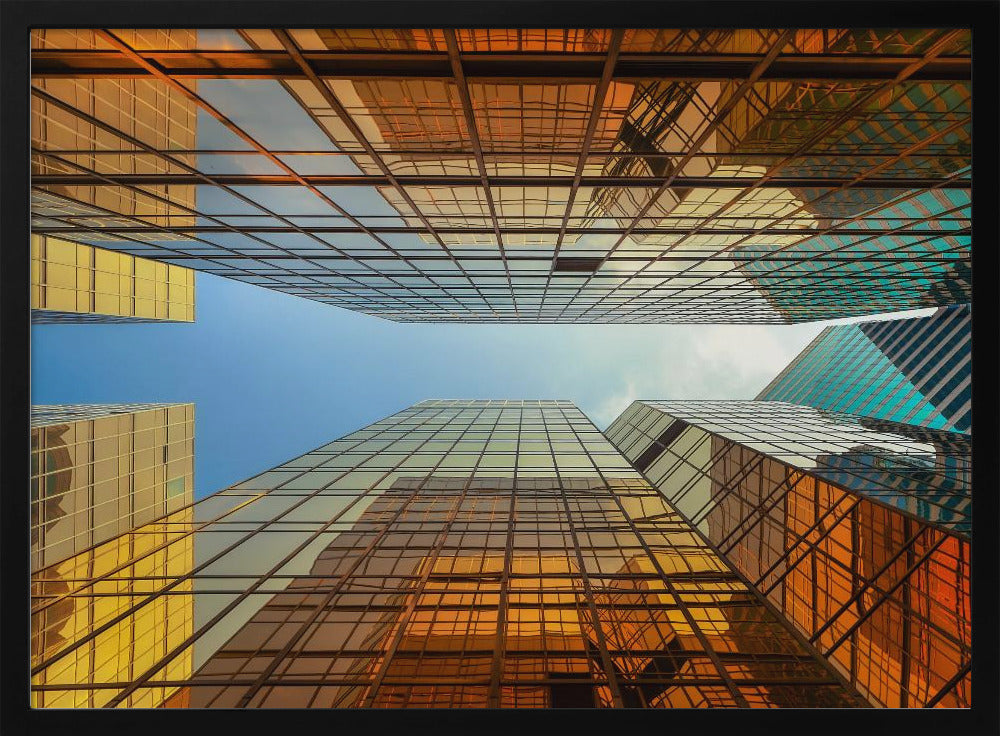 A low-angle, upward view of modern skyscrapers with golden reflective glass windows, creating a geometric pattern against a narrow strip of clear blue sky. Decor