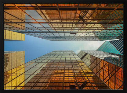 A low-angle, upward view of modern skyscrapers with golden reflective glass windows, creating a geometric pattern against a narrow strip of clear blue sky. Decor