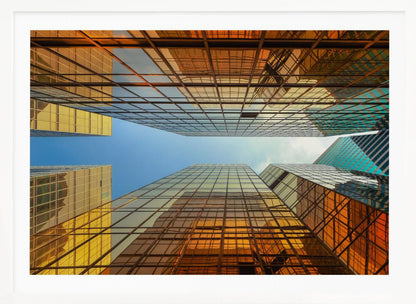 A low-angle, upward view of modern skyscrapers with golden reflective glass windows, creating a geometric pattern against a narrow strip of clear blue sky. Decor