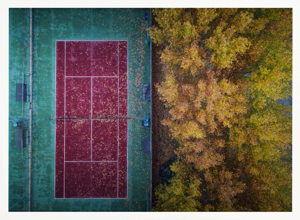 An aerial top-down photograph of a red and green tennis court covered in fallen leaves, adjacent to a dense grove of trees with vibrant yellow and gold autumn foliage, all enclosed in a silver frame. Wall Art