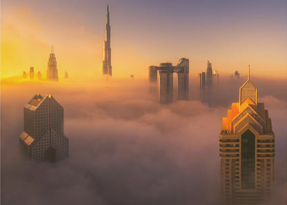 An aerial photograph of the Dubai skyline shrouded in a thick blanket of fog at sunrise. The warm golden light illuminates the tops of several skyscrapers, including the Burj Khalifa, which pierce through the clouds creating a dreamlike and majestic scene. Print