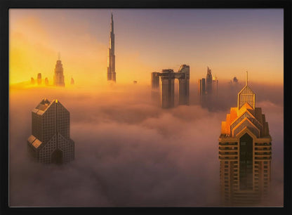 An aerial photograph of the Dubai skyline shrouded in a thick blanket of fog at sunrise. The warm golden light illuminates the tops of several skyscrapers, including the Burj Khalifa, which pierce through the clouds creating a dreamlike and majestic scene. Print