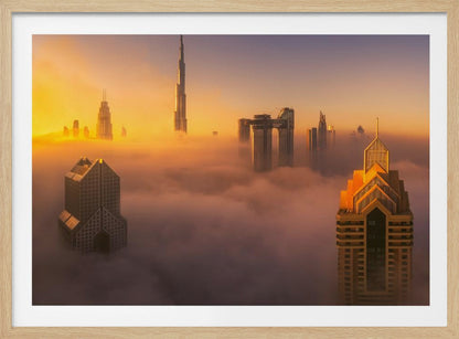 An aerial photograph of the Dubai skyline shrouded in a thick blanket of fog at sunrise. The warm golden light illuminates the tops of several skyscrapers, including the Burj Khalifa, which pierce through the clouds creating a dreamlike and majestic scene. Print
