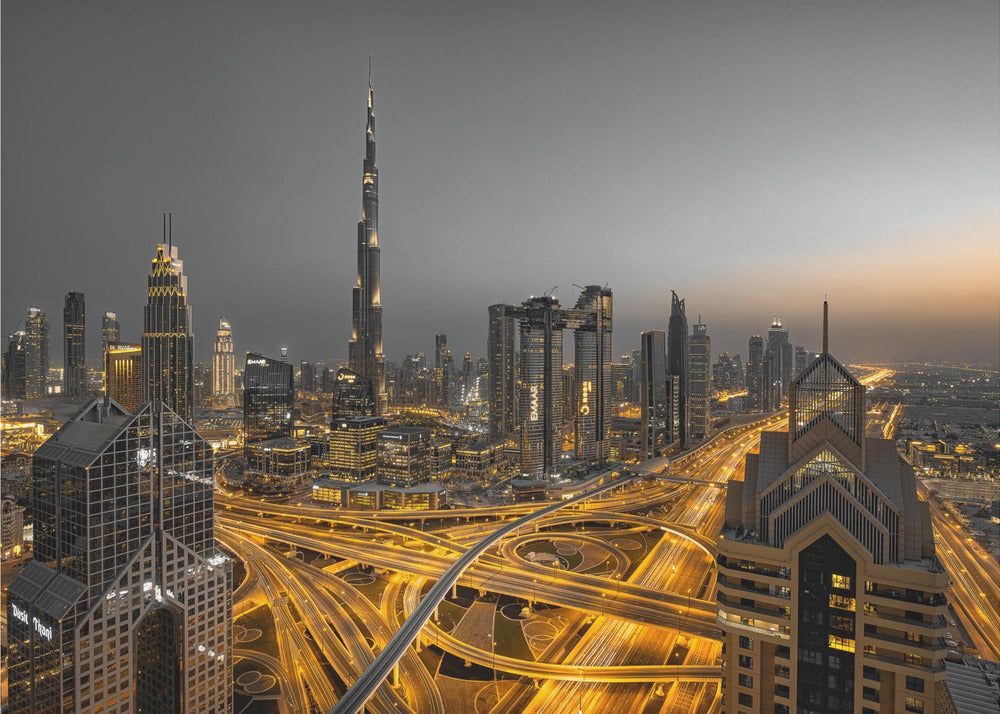 A framed, high-angle, long-exposure photograph of the Dubai skyline at dusk. The towering Burj Khalifa stands out against a grey sky, while the city's skyscrapers are illuminated. In the foreground, a complex network of highways glows with the yellow light trails of traffic, creating intricate patterns. Poster