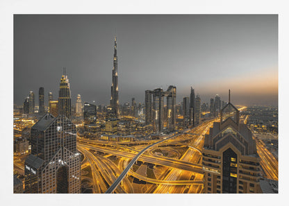 A framed, high-angle, long-exposure photograph of the Dubai skyline at dusk. The towering Burj Khalifa stands out against a grey sky, while the city's skyscrapers are illuminated. In the foreground, a complex network of highways glows with the yellow light trails of traffic, creating intricate patterns. Poster