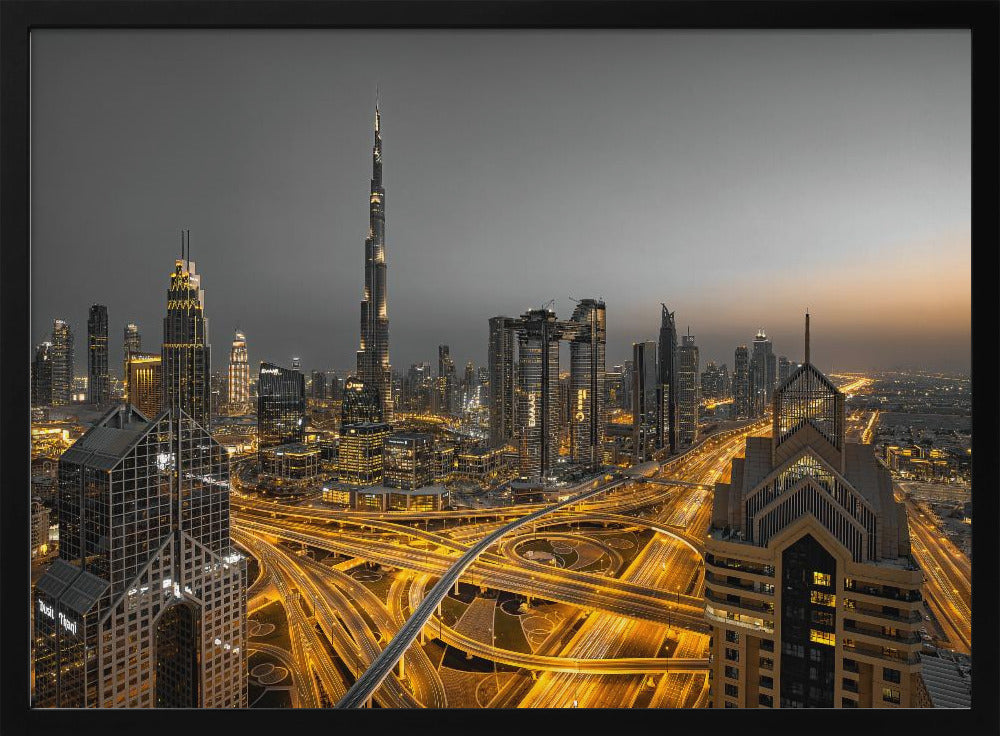 A framed, high-angle, long-exposure photograph of the Dubai skyline at dusk. The towering Burj Khalifa stands out against a grey sky, while the city's skyscrapers are illuminated. In the foreground, a complex network of highways glows with the yellow light trails of traffic, creating intricate patterns. Poster