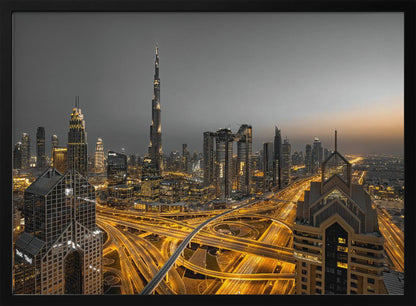 A framed, high-angle, long-exposure photograph of the Dubai skyline at dusk. The towering Burj Khalifa stands out against a grey sky, while the city's skyscrapers are illuminated. In the foreground, a complex network of highways glows with the yellow light trails of traffic, creating intricate patterns. Poster