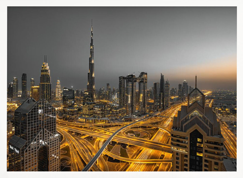 A framed, high-angle, long-exposure photograph of the Dubai skyline at dusk. The towering Burj Khalifa stands out against a grey sky, while the city's skyscrapers are illuminated. In the foreground, a complex network of highways glows with the yellow light trails of traffic, creating intricate patterns. Poster