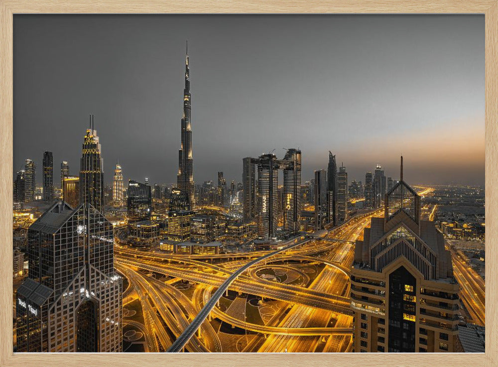 A framed, high-angle, long-exposure photograph of the Dubai skyline at dusk. The towering Burj Khalifa stands out against a grey sky, while the city's skyscrapers are illuminated. In the foreground, a complex network of highways glows with the yellow light trails of traffic, creating intricate patterns. Poster