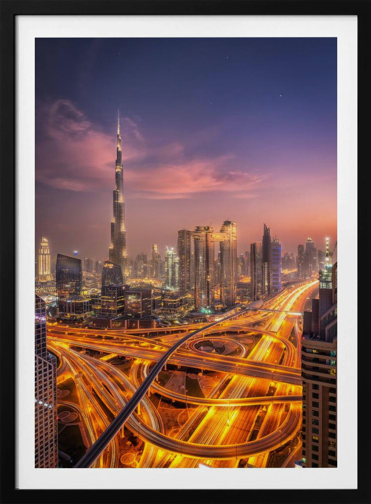 A stunning aerial photograph of the Dubai skyline at dusk, featuring the illuminated Burj Khalifa against a purple and pink sunset sky. In the foreground, complex highway interchanges are aglow with the golden-orange light trails of moving traffic, creating a sense of vibrant energy. Poster