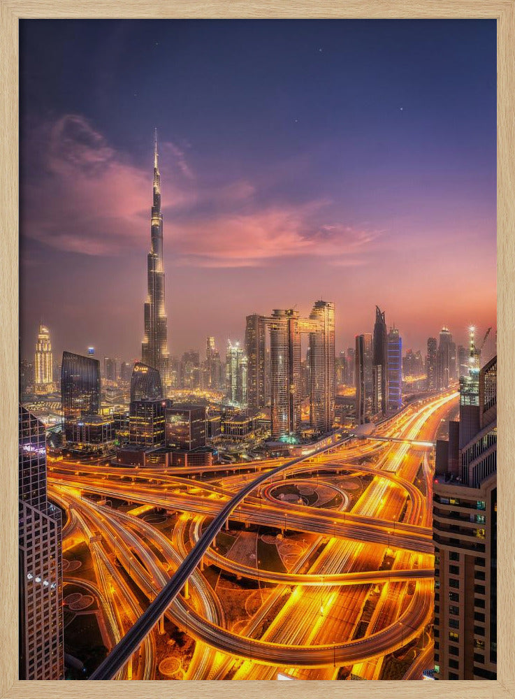 A stunning aerial photograph of the Dubai skyline at dusk, featuring the illuminated Burj Khalifa against a purple and pink sunset sky. In the foreground, complex highway interchanges are aglow with the golden-orange light trails of moving traffic, creating a sense of vibrant energy. Poster
