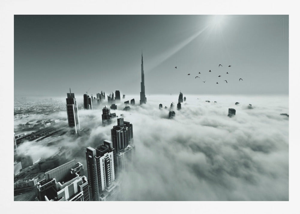A framed, black and white aerial photograph of the Dubai skyline piercing through a thick layer of clouds. The Burj Khalifa stands prominently in the center, with other skyscrapers emerging from the fog. A flock of birds flies in the sky as a bright sunbeam shines down from the upper right corner. Wall Art
