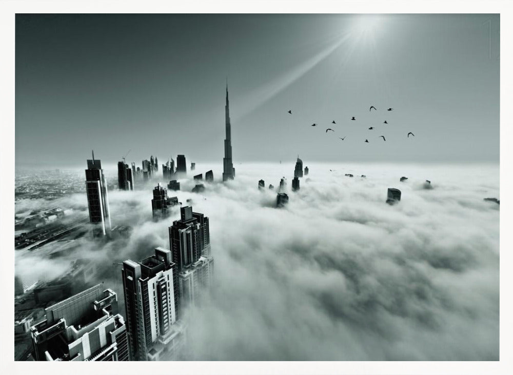 A framed, black and white aerial photograph of the Dubai skyline piercing through a thick layer of clouds. The Burj Khalifa stands prominently in the center, with other skyscrapers emerging from the fog. A flock of birds flies in the sky as a bright sunbeam shines down from the upper right corner. Wall Art