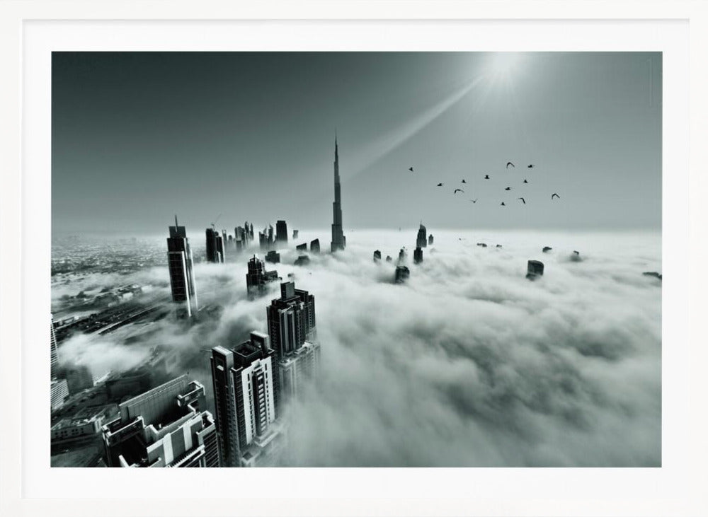 A framed, black and white aerial photograph of the Dubai skyline piercing through a thick layer of clouds. The Burj Khalifa stands prominently in the center, with other skyscrapers emerging from the fog. A flock of birds flies in the sky as a bright sunbeam shines down from the upper right corner. Wall Art